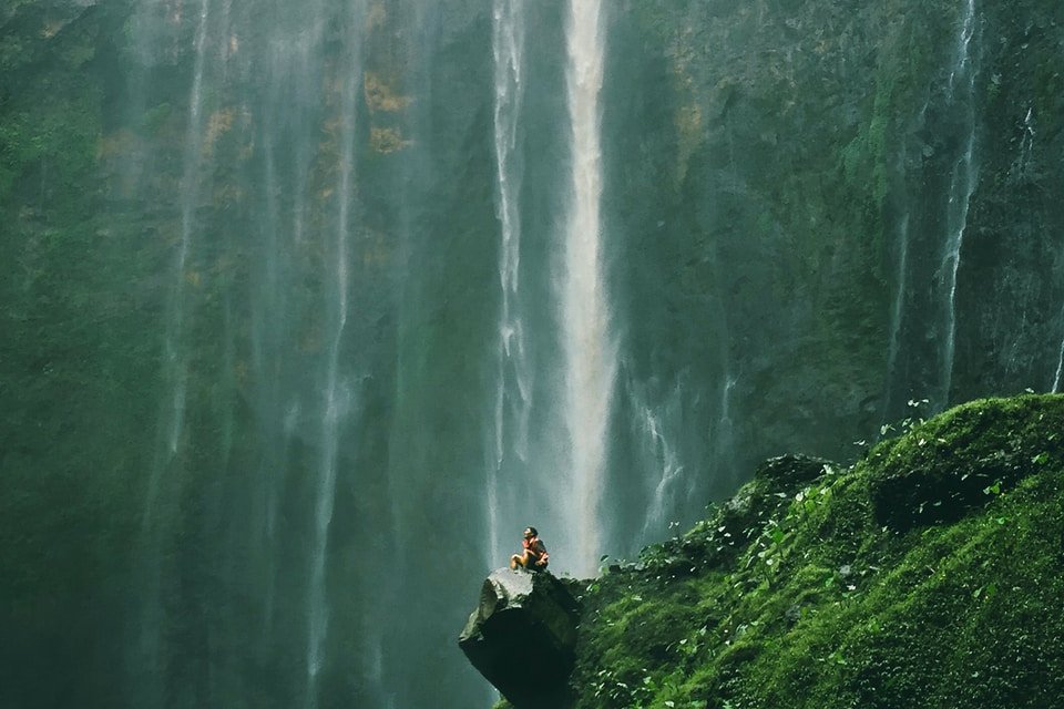 aerial photography of person sitting on rocks near waterfalls