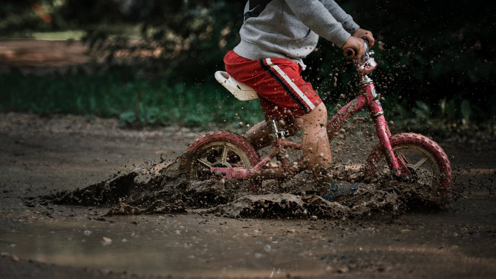 child in gray jacket and red pants riding red bicycle on brown sand during daytime