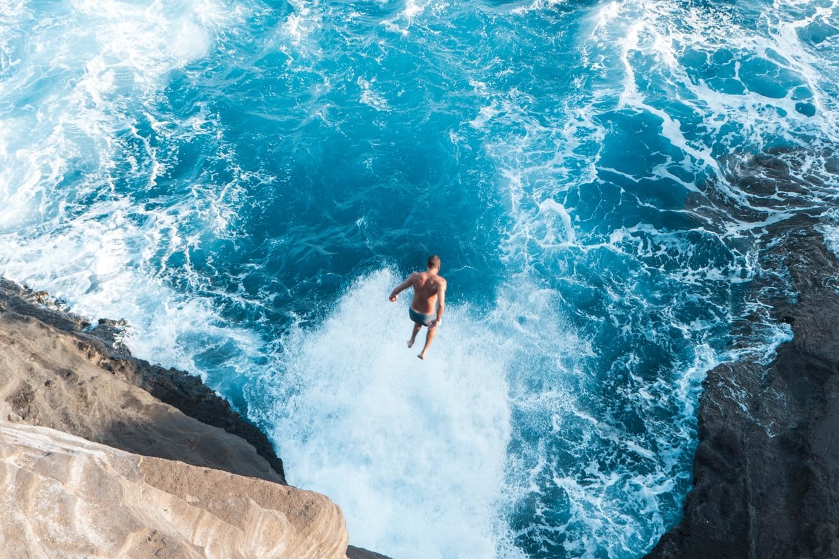 aerial photo of man jumping on cliff to the water