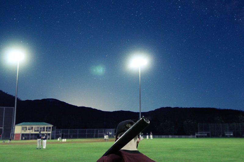 man holding baseball bat on green field