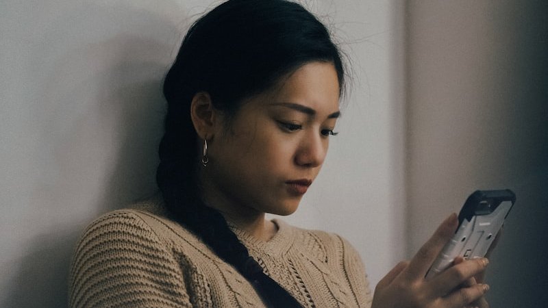 woman leaning back on white wall and using smartphone