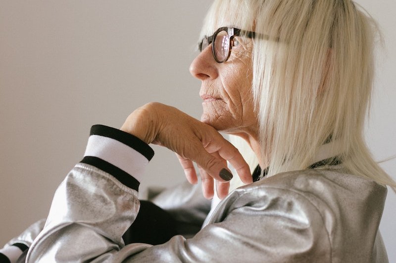 Pensive elderly woman in eyeglasses and trendy bomber