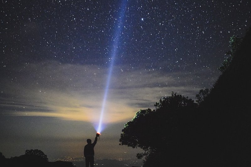 man holding flashlight pointing towards sky