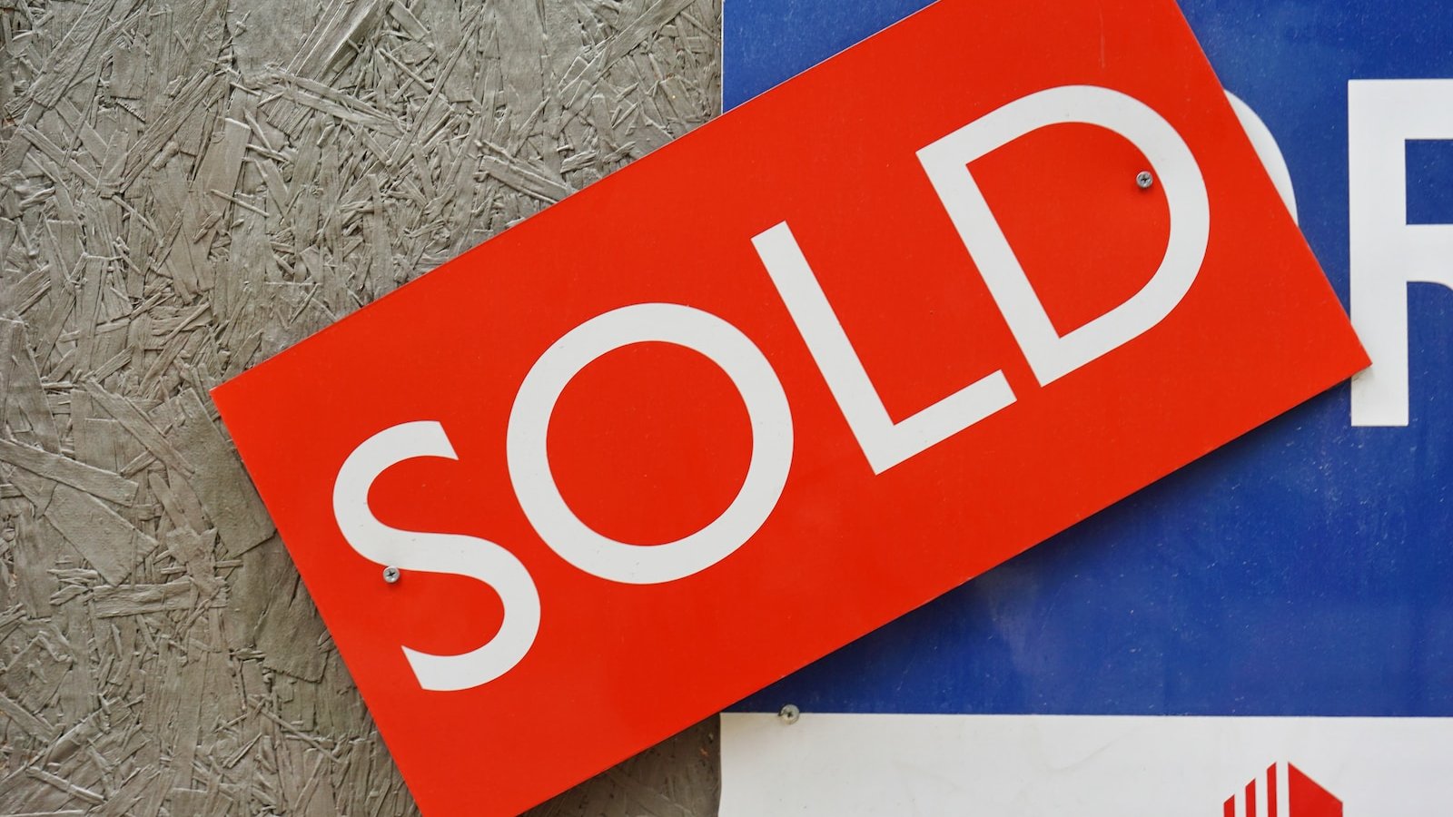 a red sold sign sitting on top of a blue sign