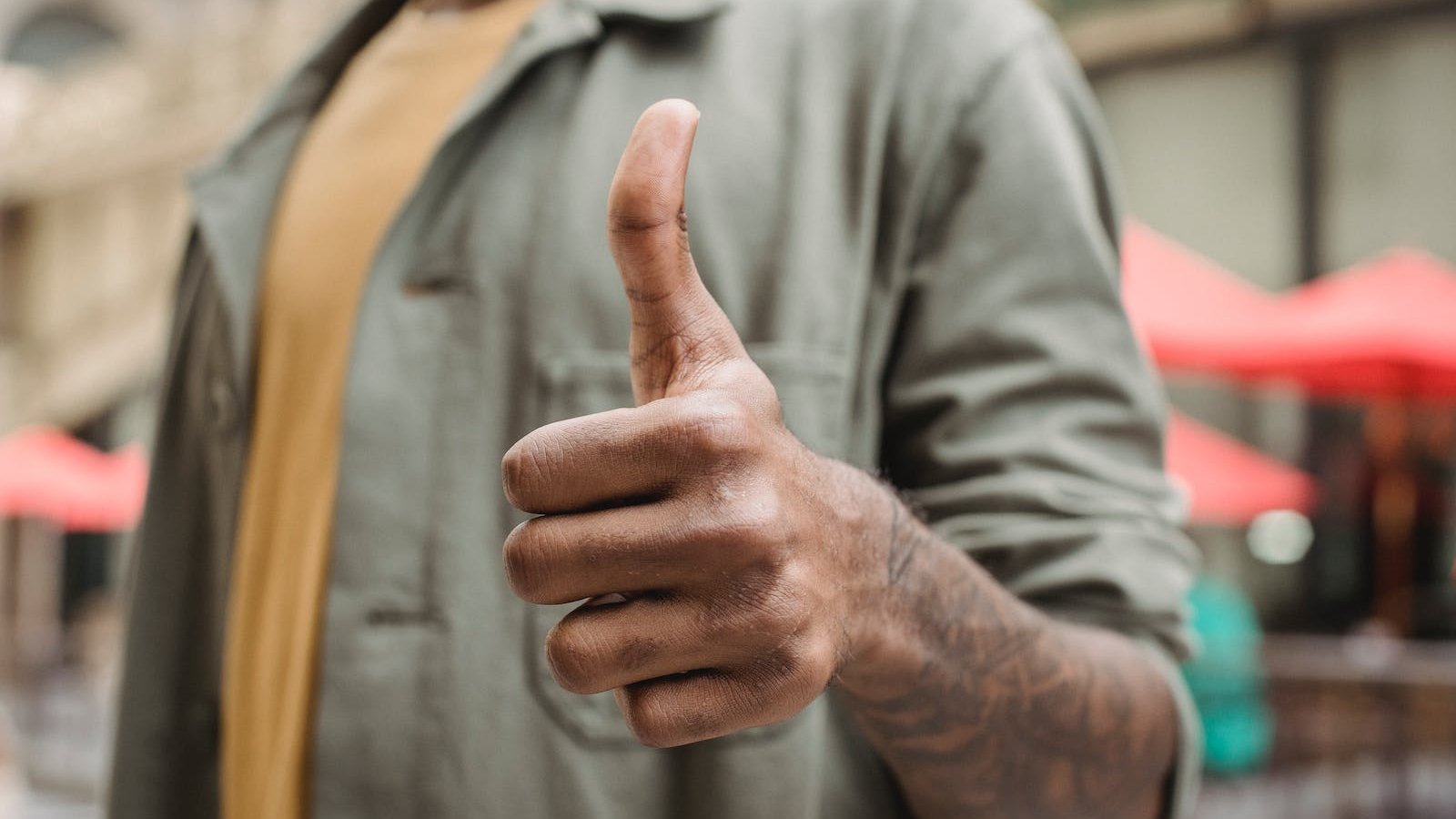 Crop faceless young black male in casual outfit standing on city street and showing thumb up gesture