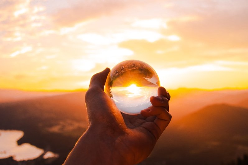 person holding glass ball reflecting sun
