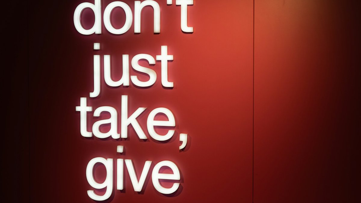 a red wall with a neon sign that says don't just take, give