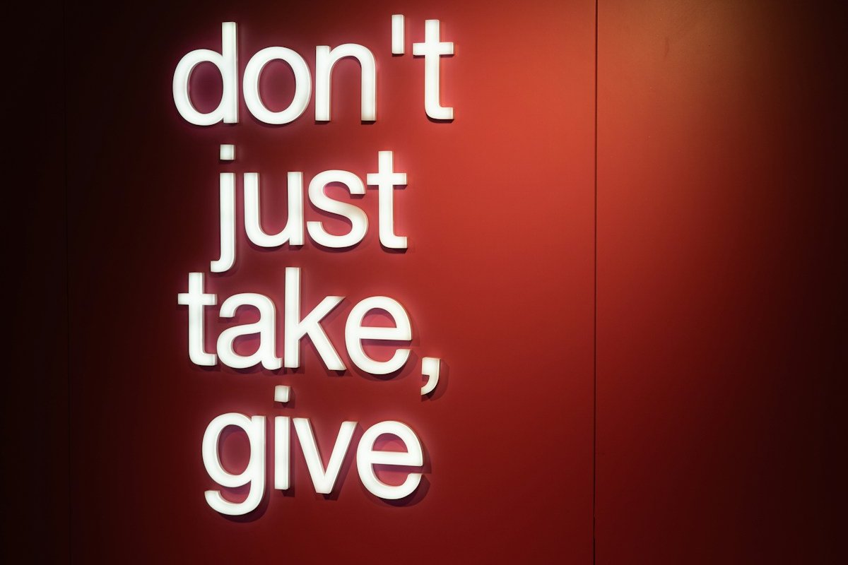 a red wall with a neon sign that says don't just take, give