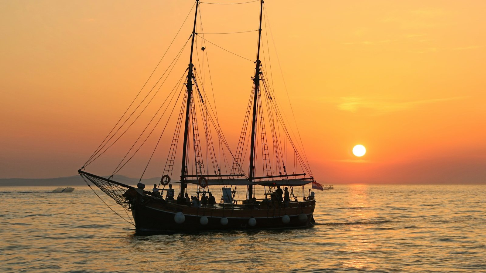 black and white sailboat in body of water during sunset