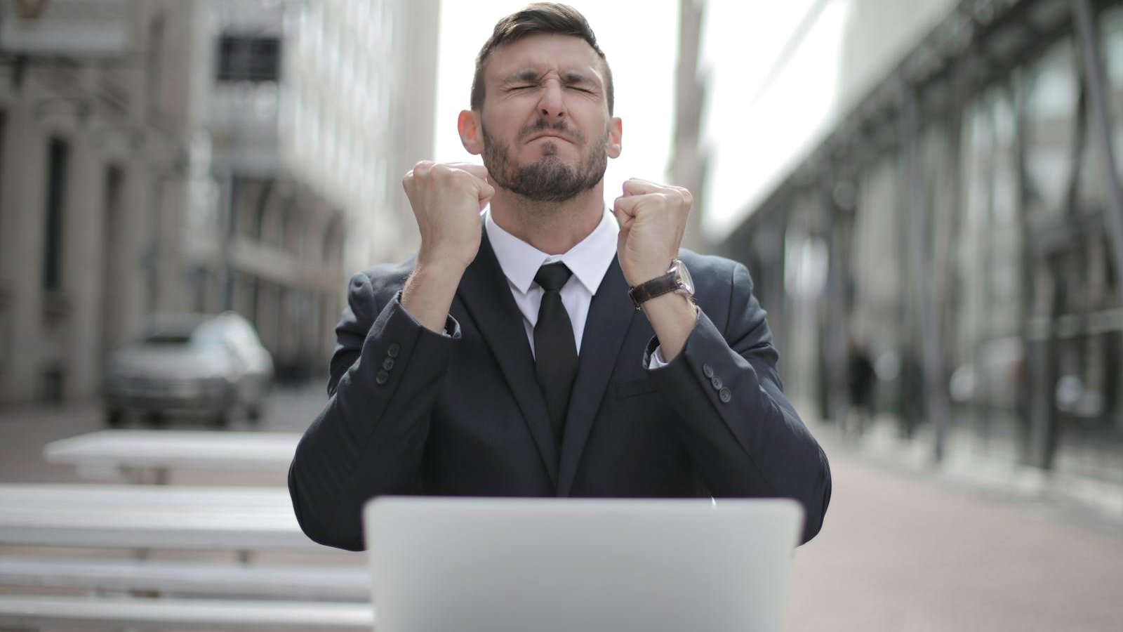 Man in Black Suit Sitting on Chair Beside Buildings