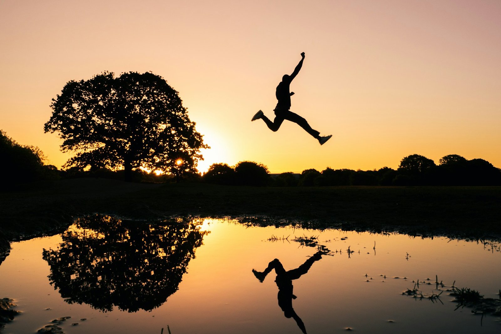 silhouette photo of man jumping on body of water during golden hour