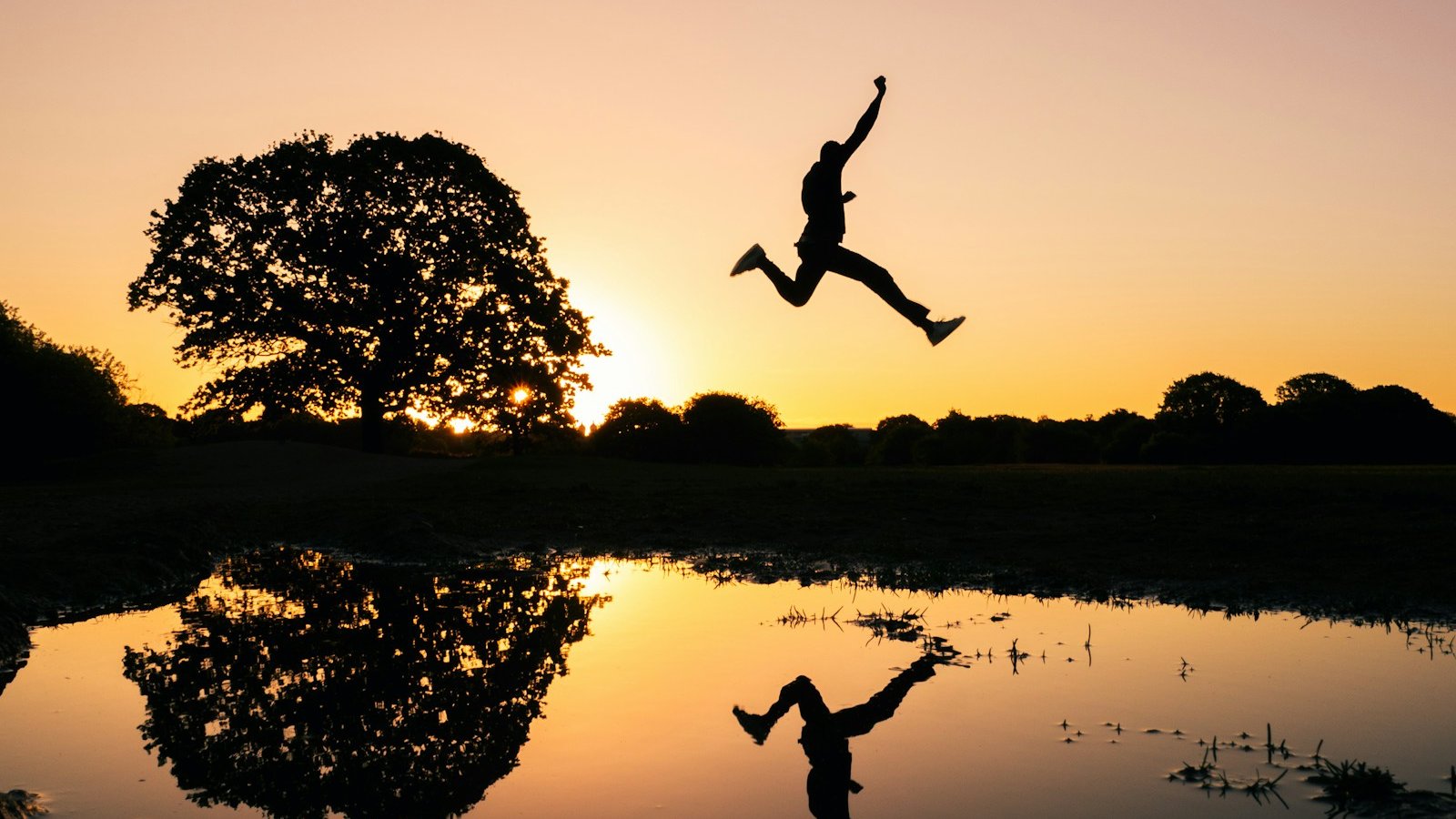 silhouette photo of man jumping on body of water during golden hour
