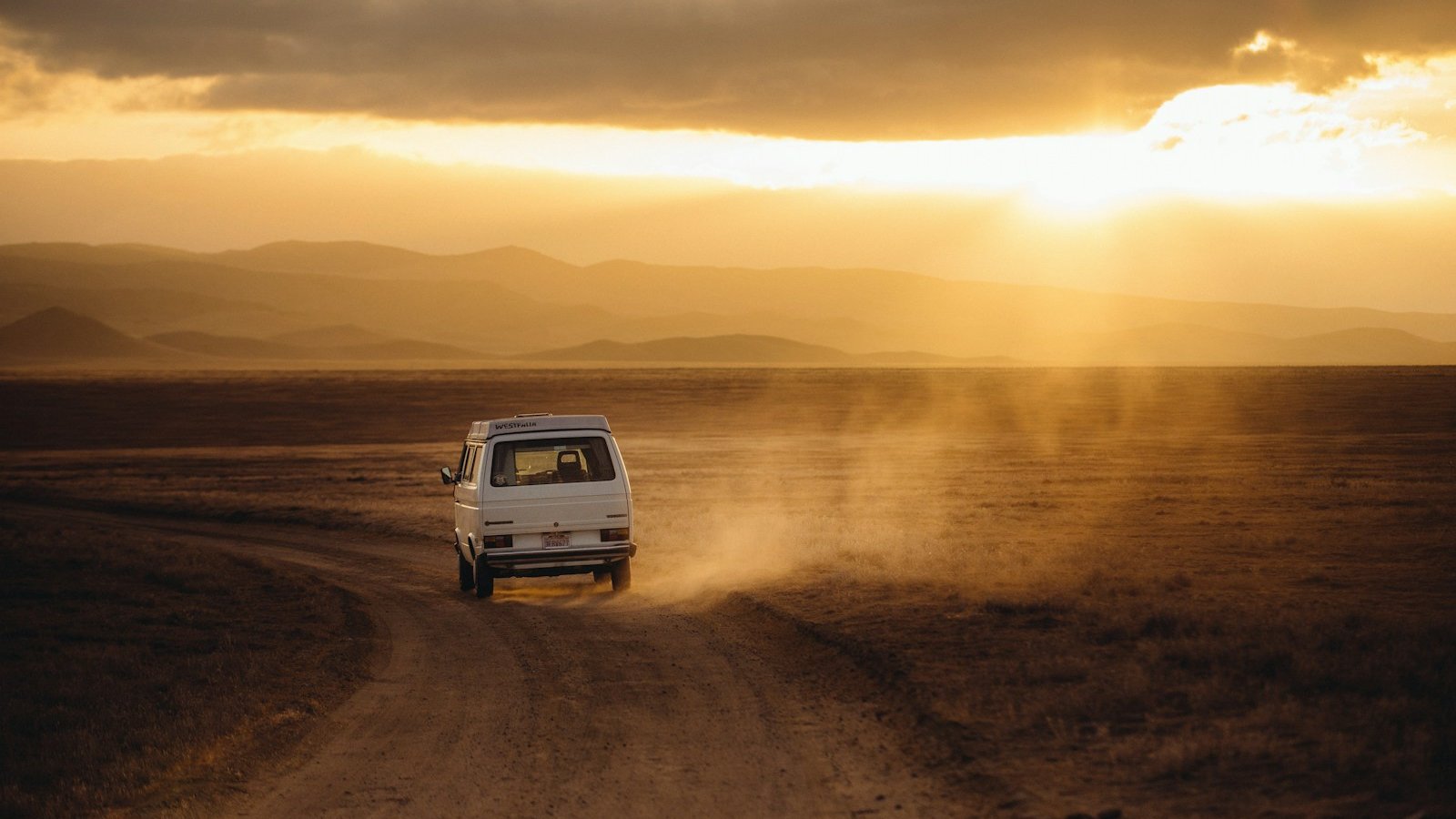 white vehicle traveling desert land field during sunset
