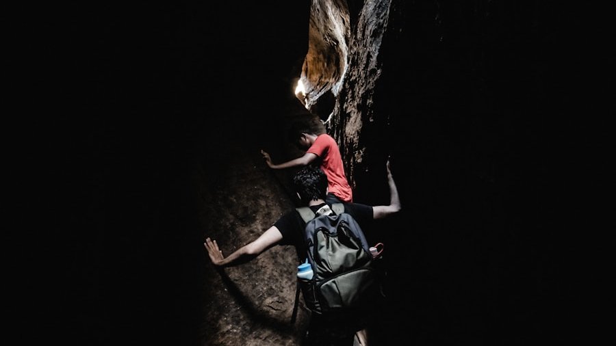 two boy's climbing between black and grey rocks during daytime