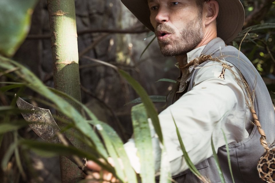man in white dress shirt and brown hat standing beside green bamboo tree during daytime