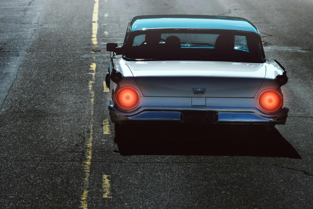 Rear view of a vintage car with bright tail lights driving on an empty road.