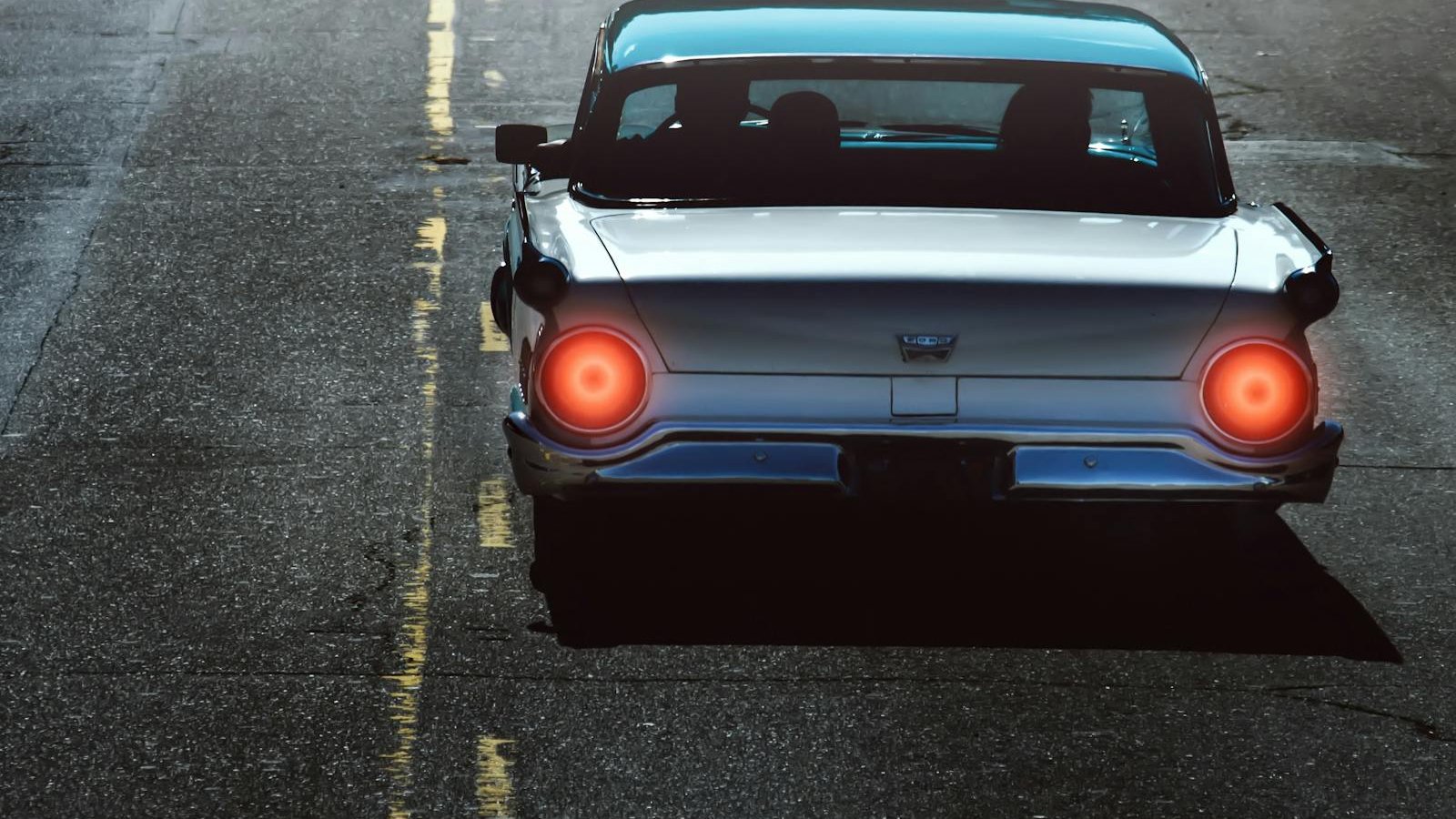 Rear view of a vintage car with bright tail lights driving on an empty road.