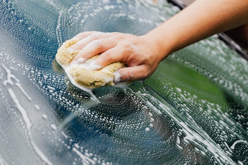 Close-up of a hand washing a car windshield with a soapy sponge, detailing care.