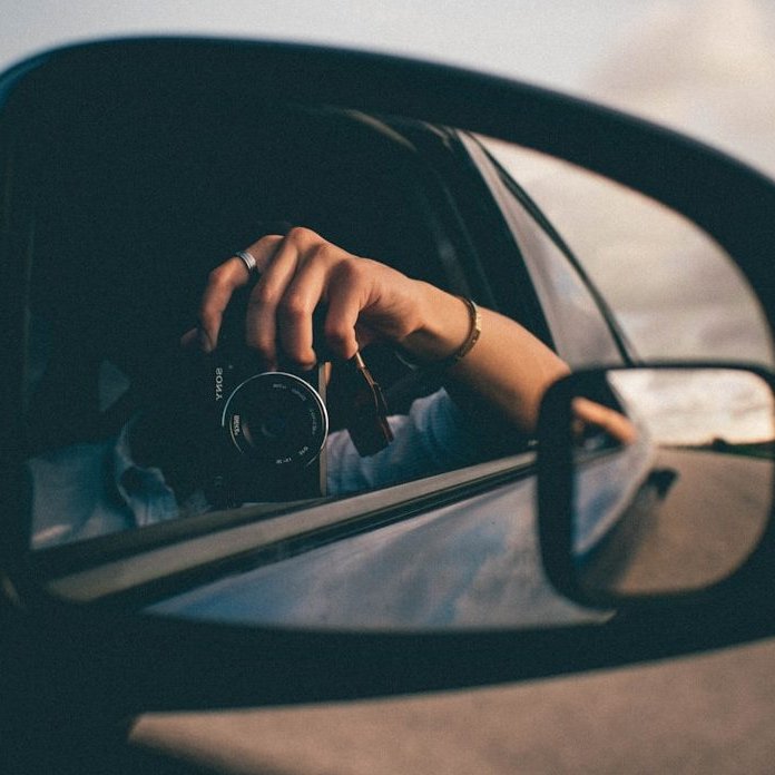 person using camera at the side mirror